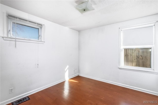 unfurnished room featuring baseboards, wood-type flooring, a textured ceiling, and visible vents