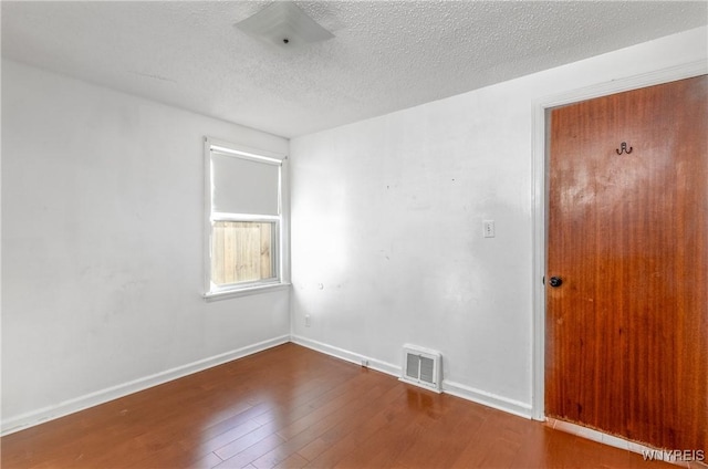 spare room featuring baseboards, visible vents, wood-type flooring, and a textured ceiling