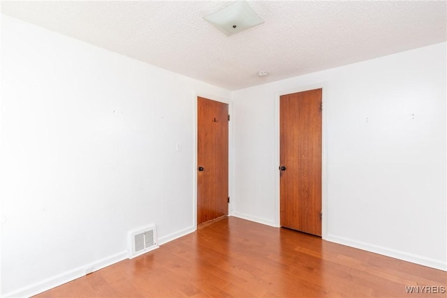 empty room featuring baseboards, wood finished floors, visible vents, and a textured ceiling