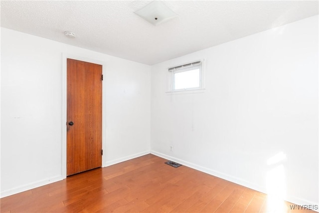 empty room featuring visible vents, baseboards, a textured ceiling, and wood finished floors