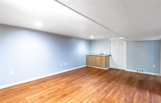 basement featuring indoor wet bar, light wood-style flooring, baseboards, and a sink