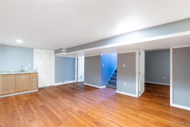 finished below grade area featuring light wood finished floors, stairway, baseboards, and a sink