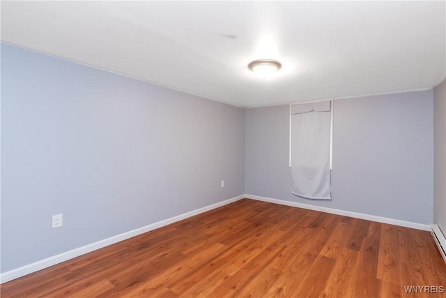 spare room featuring a baseboard heating unit, baseboards, and wood finished floors