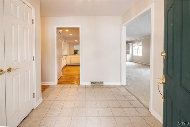 entrance foyer with light tile patterned floors, visible vents, light colored carpet, and baseboards