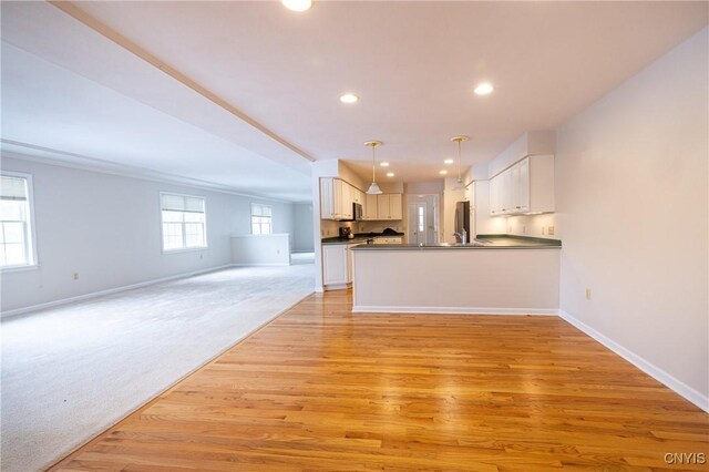 interior space with dark countertops, light wood finished floors, baseboards, open floor plan, and pendant lighting