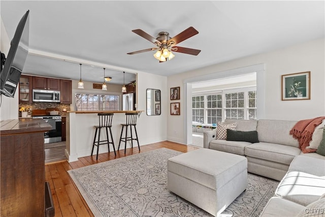 living area featuring a ceiling fan, light wood-style floors, and baseboards