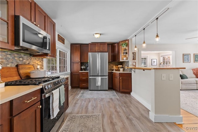 kitchen featuring backsplash, open floor plan, light wood-type flooring, a peninsula, and stainless steel appliances