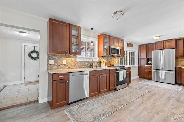 kitchen featuring decorative backsplash, light countertops, glass insert cabinets, appliances with stainless steel finishes, and light wood-type flooring