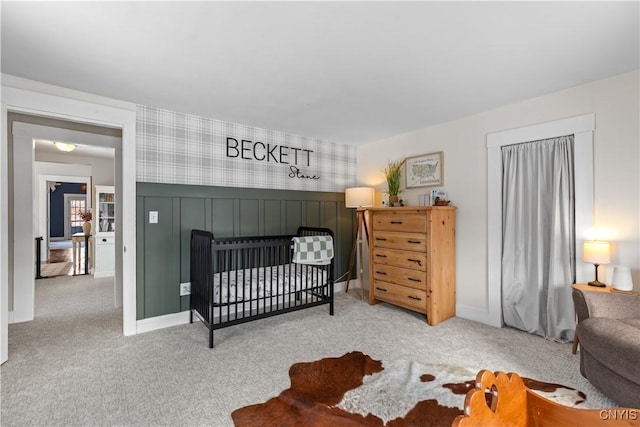 bedroom with wallpapered walls, a nursery area, a wainscoted wall, and carpet floors