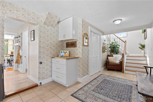 interior space featuring light tile patterned floors, stairway, wallpapered walls, and a textured ceiling