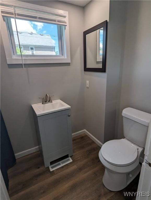 half bath with visible vents, toilet, wood finished floors, baseboards, and vanity