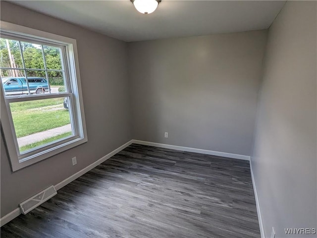 spare room with dark wood finished floors, visible vents, and baseboards