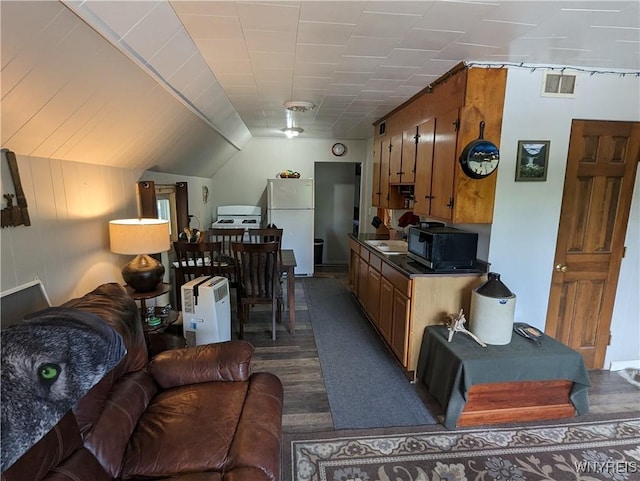 kitchen with brown cabinetry, visible vents, freestanding refrigerator, black microwave, and dark countertops