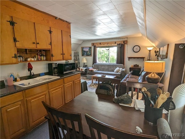 kitchen with dark countertops, black microwave, open floor plan, lofted ceiling, and a sink