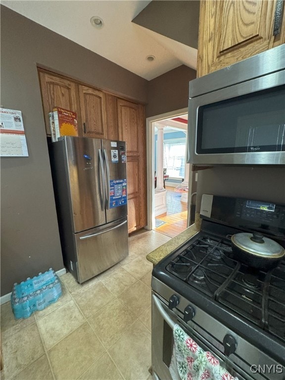 kitchen featuring stainless steel appliances, brown cabinetry, light tile patterned floors, baseboards, and ornate columns