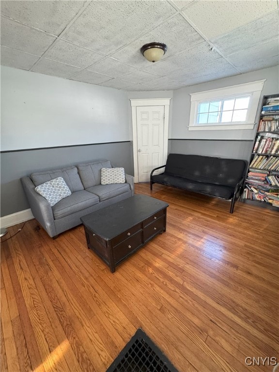 living area with a drop ceiling, baseboards, and light wood finished floors