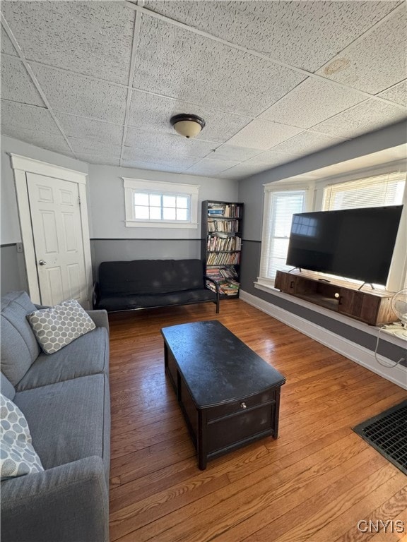 living area featuring a drop ceiling, a healthy amount of sunlight, and wood finished floors