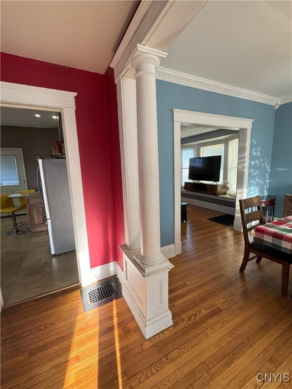 hall featuring wood finished floors, baseboards, visible vents, decorative columns, and ornamental molding