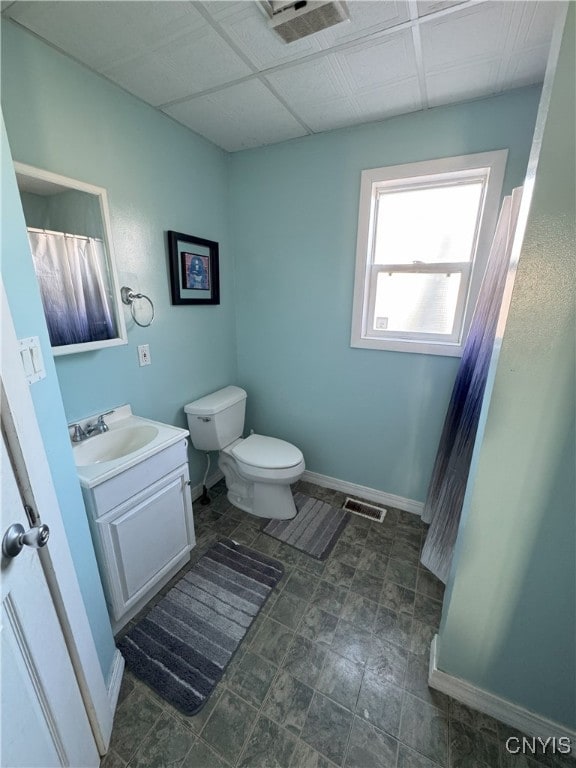 bathroom featuring visible vents, baseboards, a drop ceiling, toilet, and vanity