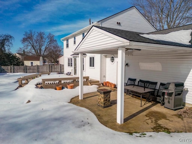 snow covered back of property featuring a patio, an outdoor living space with a fire pit, roof with shingles, and fence