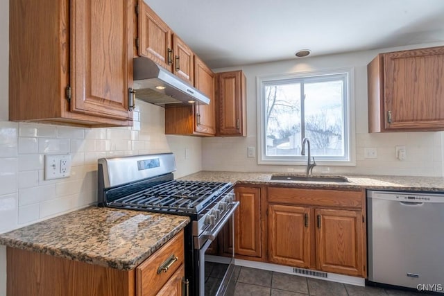 kitchen with under cabinet range hood, brown cabinets, appliances with stainless steel finishes, and a sink