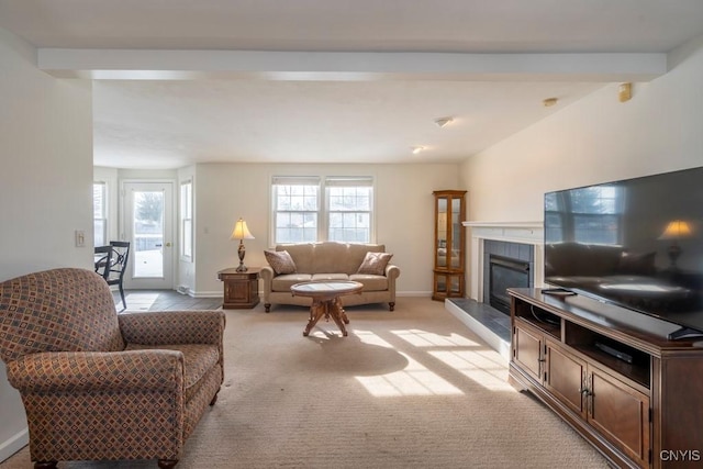 living room with a wealth of natural light, light colored carpet, a tiled fireplace, and baseboards