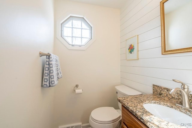 bathroom with vanity, toilet, visible vents, and wood walls