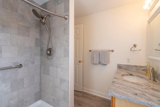 bathroom with a tile shower, vanity, baseboards, and wood finished floors