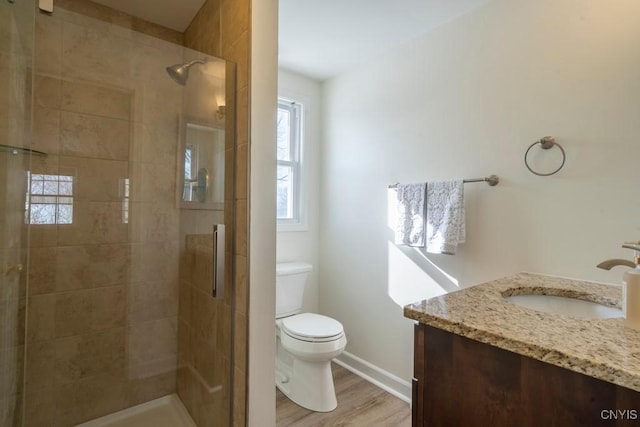 bathroom with toilet, a stall shower, wood finished floors, baseboards, and vanity