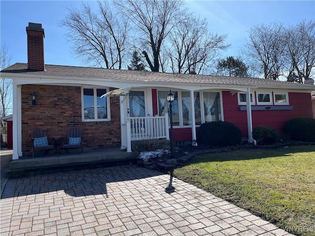 single story home with brick siding, a front yard, covered porch, and a chimney