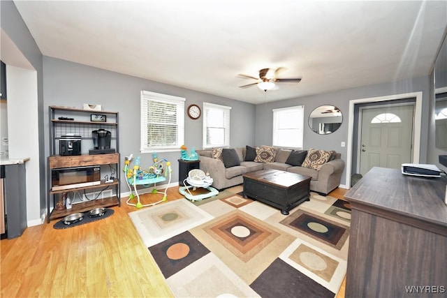 living area with a ceiling fan, light wood-type flooring, and baseboards