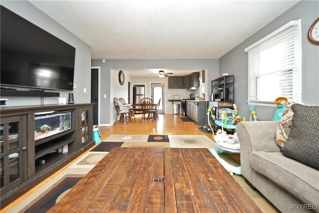 living area with light wood-type flooring, baseboards, a healthy amount of sunlight, and a ceiling fan