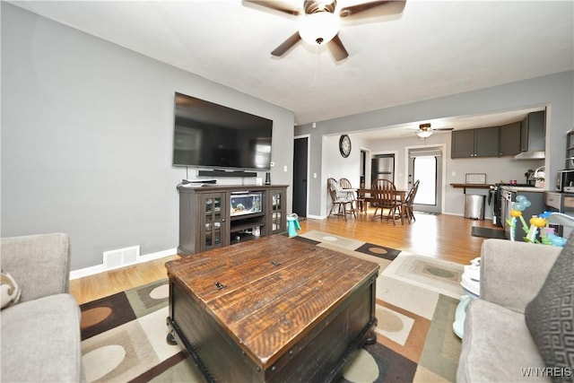 living area featuring a ceiling fan, wood finished floors, visible vents, and baseboards