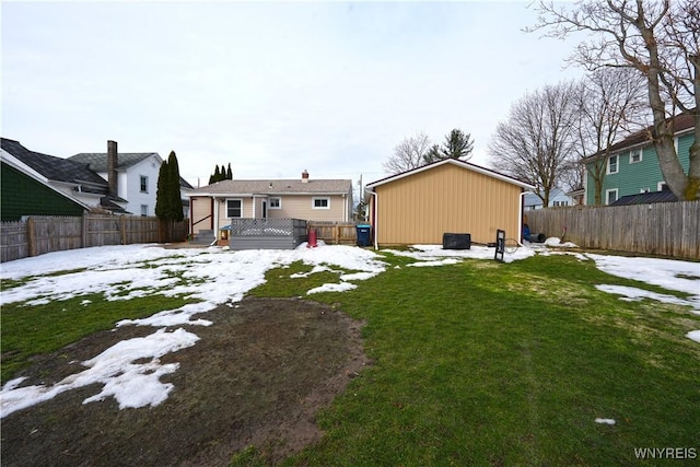 snow covered rear of property with a wooden deck, an outbuilding, a lawn, and a fenced backyard