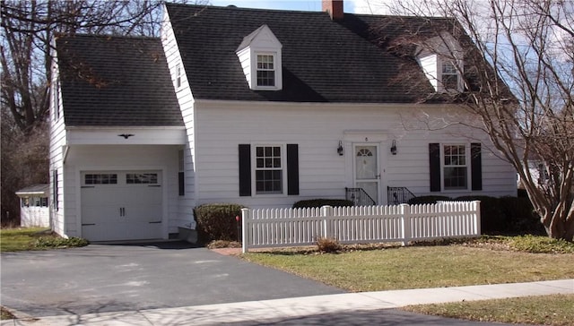 cape cod house featuring roof with shingles, a chimney, a garage, a fenced front yard, and aphalt driveway