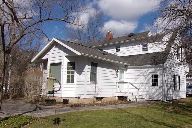 back of house featuring a lawn, a chimney, and roof with shingles