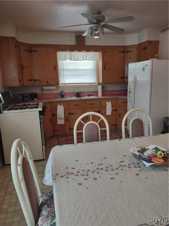 kitchen with a ceiling fan, a sink, wallpapered walls, white appliances, and light countertops