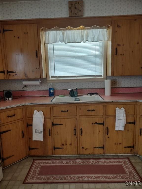 kitchen featuring wallpapered walls, light countertops, light floors, and a sink