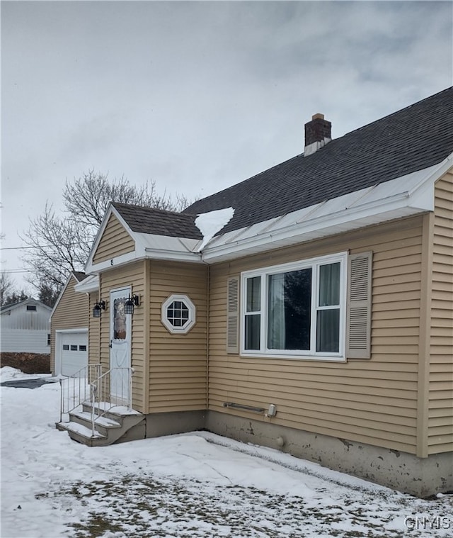 view of front of house featuring entry steps, an attached garage, roof with shingles, and a chimney