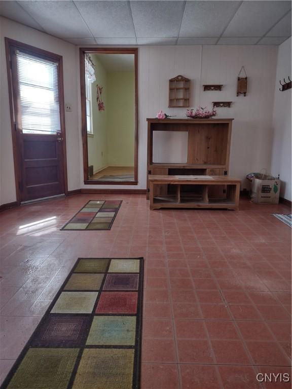 unfurnished living room featuring a paneled ceiling and baseboards