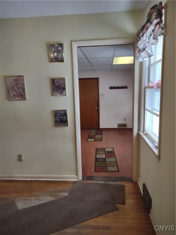 corridor featuring visible vents, a paneled ceiling, baseboards, and wood finished floors