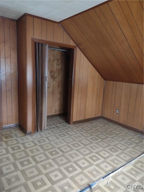 bonus room featuring vaulted ceiling, wooden walls, and baseboards