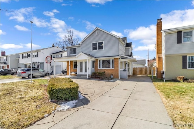 view of front of house featuring fence, a residential view, concrete driveway, a front lawn, and brick siding