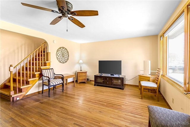 living area featuring light wood-type flooring, baseboards, ceiling fan, and stairs