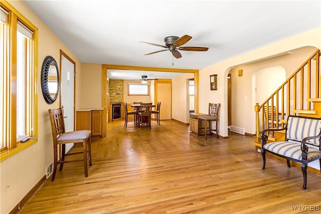 sitting room featuring stairway, baseboards, light wood finished floors, arched walkways, and ceiling fan