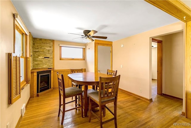 dining area featuring light wood-type flooring, visible vents, a large fireplace, baseboards, and ceiling fan