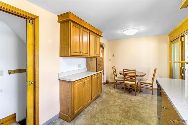 kitchen featuring arched walkways, brown cabinets, baseboards, and light stone countertops