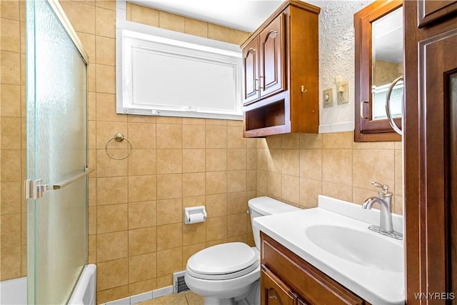 full bathroom with vanity, tile walls, toilet, and bath / shower combo with glass door