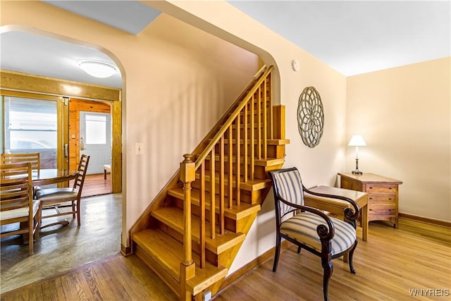 staircase featuring arched walkways, baseboards, and hardwood / wood-style floors