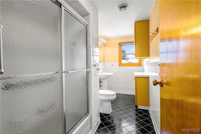 full bath with tile patterned floors, a shower with shower door, toilet, tile walls, and wainscoting